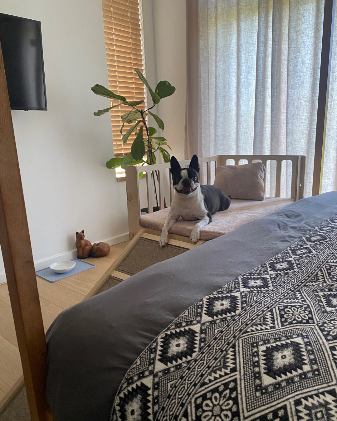 Dog using a wooden bedside dog bed positioned next to the owner's bed