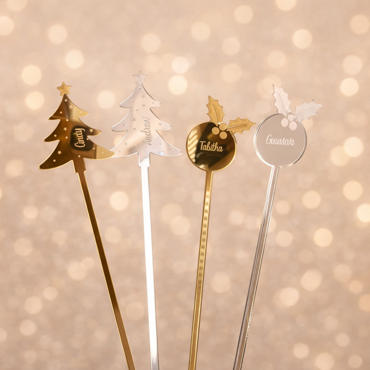 Three personalised acrylic Christmas drink stirrers in festive designs against a soft golden background