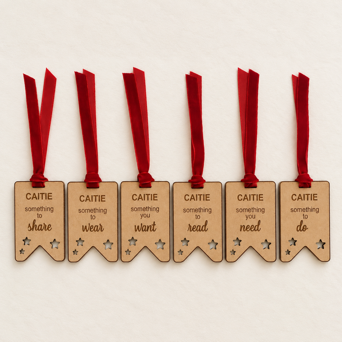 Set of six personalised wooden Christmas gift tags engraved with Caitie, featuring star-shaped cutouts and red velvet ribbons.
