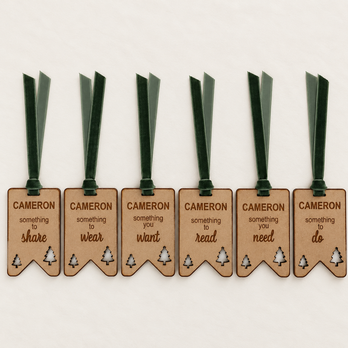 Set of six personalised wooden Christmas gift tags engraved with Cameron, featuring Christmas tree cutouts and green velvet ribbons.